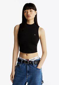 Sort crop top med høj hals, der har et logo-detalje, parret med højtaljede blå jeans og et sort bælte med en sølvspænde.