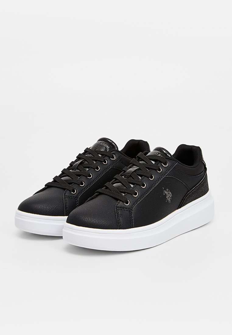 Baskets noires avec une tige en cuir texturé, semelle en caoutchouc blanche et lacets noirs. Présente un logo sur le côté et des accents métalliques.