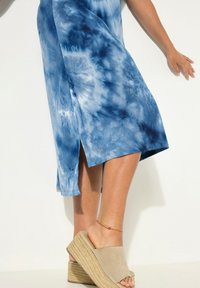 Modrá tie-dye šaty s bočním rozparkem, vyrobené z lehkého materiálu. V kombinaci s béžovými klínovými sandály s texturovanou podrážkou.