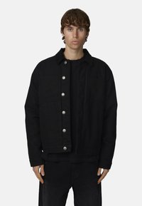 Giubbotto di jeans nero con bottoni a pressione argento, colletto e due tasche frontali, caratterizzato da un tessuto testurizzato e una vestibilità comoda.