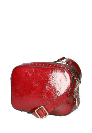 Petit sac bandoulière en cuir rouge brillant avec bandoulière réglable, clous argentés le long du bord supérieur et fermeture éclair argentée.