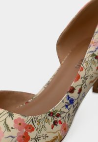Chaussure à talon haut à motif floral avec des fleurs roses, rouges et bleues sur un fond beige et une doublure intérieure beige.