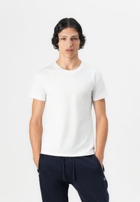 Hvid kortærmet t-shirt lavet af blødt bomuld, med en klassisk rund halsudskæring og en skræddersyet pasform. Båret med mørkeblå bukser.