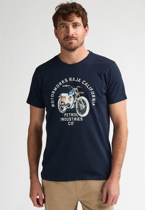 Marineblauw katoenen T-shirt met een afbeelding van een motorfiets. Het ontwerp bevat witte en gekleurde tekst: "MOTORWORKS BAJA CALIFORNIA" en "PETROL INDUSTRIES CO."