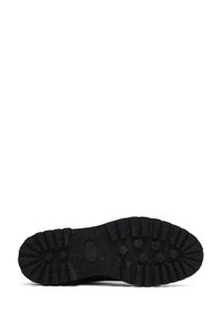 Semelle de chaussure en caoutchouc noir avec un motif de grip texturé, comportant des crampons prononcés et un logo ovale central. Design durable et antidérapant.
