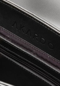 Portafoglio nero con esterno in faux leather liscio. Presenta un interno testurizzato con un compartimento con zip e il logo "AKARDO" impresso.