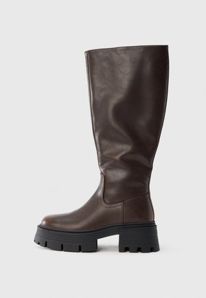 Botte haute jusqu'au genou en cuir marron avec une semelle noire épaisse, texture lisse, bout rond et détails de couture minimaux.