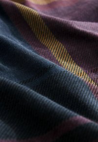 Textil mit einem gewebten Muster aus gestreiften in dunklem Marineblau, Burgunderrot und Gelb. Weiche Textur mit einem leichten Glanz, der die Tiefe betont.