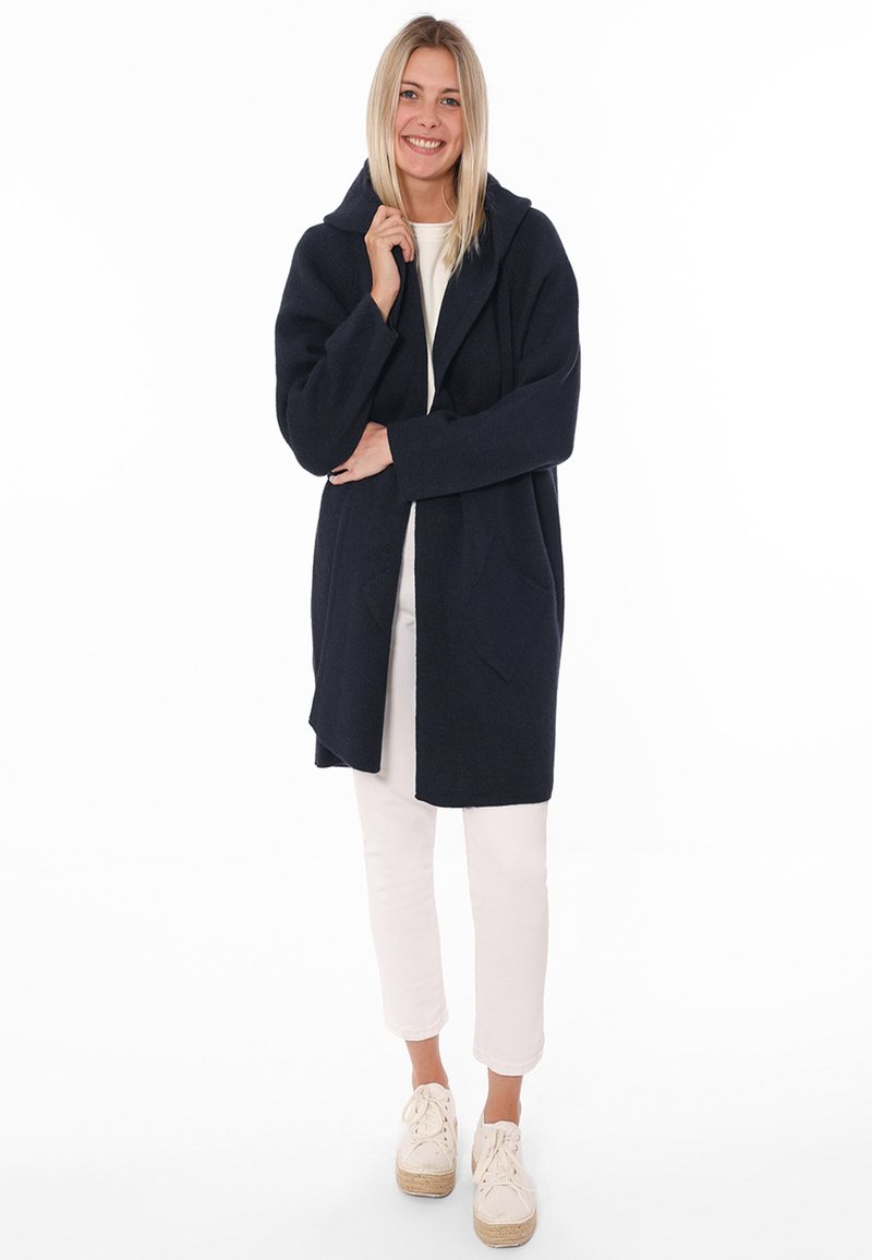 Cappotto in lana blu navy con cappuccio, maniche lunghe e ampie tasche frontali. Design morbido con finitura texturizzata.
