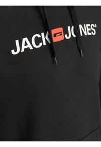 Svart hoodie med vit text "JACK" och "JONES", med en röd ruta. Inkluderar dragsnören och texturerad tyg. Inga synliga mönster eller accenter.