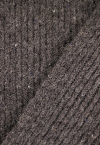 Szara dzianina o strukturalnym, żeberkowym wzorze; zawiera różnorodne włókna, co nadaje jej lekko puszysty wygląd. Bogaty i ciepły odcień kolorystyczny.