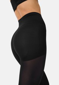 Hochtaillierte schwarze Leggings mit glatter Textur, die im unteren Abschnitt semi-transparent und mit einem nahtlosen Bunddesign versehen sind.