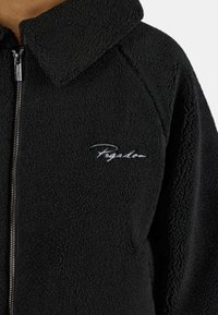 Giacca in pile nera con zip frontale, grande colletto e superficie testurizzata. Presenta il logo ricamato bianco "Pegadon" sul petto.