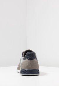 Szare zamszowe sneakersy z czarnym teksturowanym obcasem, białą gumową podeszwą i jasnoszarymi akcentami. Posiadają wyściełany kołnierz i kontrastowe szwy.