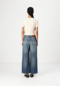 Κρέμα ριμπ μπλούζα κοντό μανίκι συνδυασμένη με παντελόνι τζιν φαρδύ πόδι σε μπλε, με πίσω τσέπες και δερμάτινη ετικέτα στη μέση.