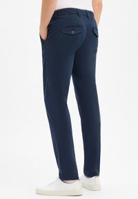 Pantalons stretch bleu marine à coupe ajustée, dotés de poches latérales, d'une poche arrière avec bouton et d'une texture douce. Associés à des baskets blanches.