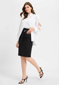 Weißes Hemd mit Knöpfen und ausgeschnittenen Ärmeln, kombiniert mit einem schwarzen Bleistiftrock mit silberner Kettenakzentuierung. Schwarze Riemchenabsätze vervollständigen den Look.