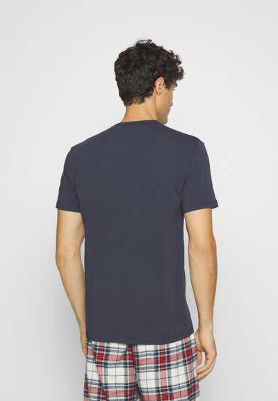 Navy blue cotton t-shirt with a crew neckline, short sleeves, and a relaxed fit; model wears plaid pajama pants.