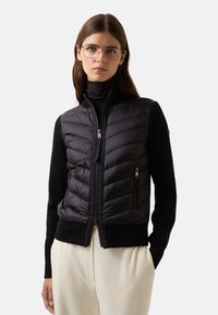 Czarna pikowana kamizelka z prążkowanym dzianinowym ciałem, z zamykanymi na zamek kieszeniami i stójką, charakteryzująca się eleganckim designem i kontrastującymi fakturami.