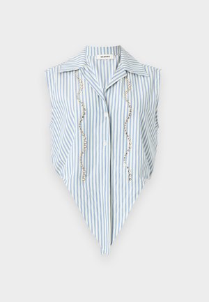 Nő világoskék csíkos ujjatlan kötött ingben, fehér magasderekú rövidnadrágban, sötétbarna kézitáskával a kezében, barna bojtos mokaszinban.