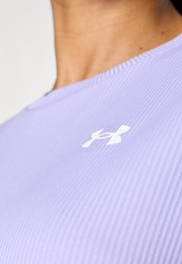 Levendula színű sportpóló bordás textúrával, bal oldalon, a mellkas fölött fehér Under Armour logóval.