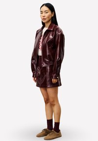 Bordeaux faux leren jack met een rits aan de voorkant, gecombineerd met een bijpassende rok. Bruine textuur schoenen en enkel sokken maken de outfit compleet.