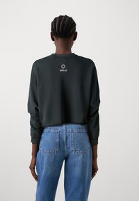 Sudadera negra recortada con mangas largas, con un pequeño logotipo blanco en la parte trasera. Combinada con unos jeans de mezclilla azul claro de cintura alta.