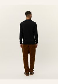 Zwarte lange mouwen shirt gezien vanaf de achterkant, gecombineerd met een broek van bruine corduroy. De textuur van het shirt is glad, terwijl de broek ribbelig is.