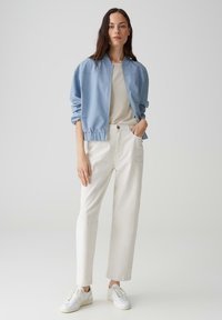 Veste bomber bleu clair, top beige, pantalon blanc taille haute et baskets blanches, présentant une tenue décontractée avec une coupe confortable.