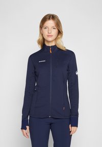 Marineblaue, langärmelige Jacke mit hohem Kragen, strukturiertem Stoff, Frontreißverschluss und orangefarbenem Zipper. Mit Logo auf Brust und Ärmel.
