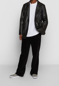 Svart läderblazer, vit t-shirt, svarta kordflorsebyxor och rutiga slip-on-skor. Slät textur med en något avslappnad passform.