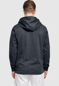 Mørkegrå hættetrøje med en stor, justerbar hætte. Har lange ærmer, ribbet kant og en glat tekstur. Ingen synlig branding.
