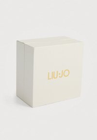 Λευκό κουτί με υφή και με το χρυσό λογότυπο "LIU·JO" στο μπροστινό μέρος. Τετράγωνο σχήμα, καθαρός σχεδιασμός, χωρίς πρόσθετα μοτίβα ή διακοσμήσεις.