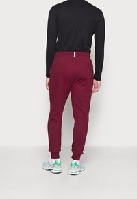 Bordeauxfarbene Jogginghosen aus weichem Stoff verfügen über ein schmal zulaufendes Design, einen elastischen Bund mit tricolor Akzent und seitliche Taschen.
