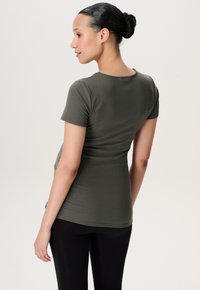 Olivengrøn, kortærmet ribbet top, tætsiddende silhuet, blød tekstur, rund halsudskæring, bæres med sorte leggings, ensfarvet baggrund.