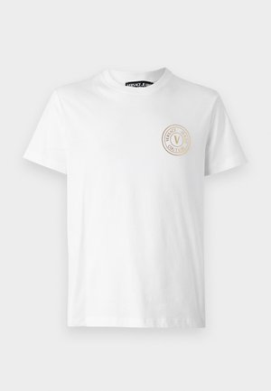 T-shirt bianco in cotone con scollatura rotonda e maniche corte, caratterizzato da un logo circolare dorato nella zona sinistra del petto.