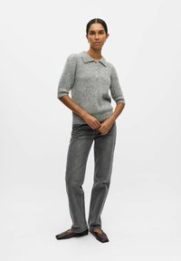 Grauer Strick-Polo-Pullover mit kurzen Ärmeln und drei Knöpfen, kombiniert mit grauen Jeans und braunen flachen Schuhen.