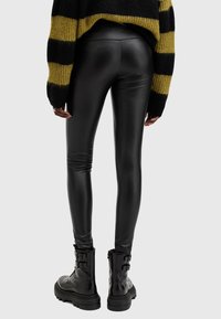 Leggings neri in ecopelle con una texture liscia, sagomati e di lunghezza ankle, abbinati a stivali combat chunky neri opachi.