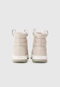 Bottes imperméables beiges avec une cheville rembourrée, présentant un design rembourré et le logo Techlite sur la semelle. Deux languettes à l'arrière.