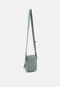Svetlomodrá crossbody taška z látky s obdĺžnikovým tvarom, nastaviteľný popruh, zips a mäkkú textúru. Kompaktný a minimalistický dizajn.