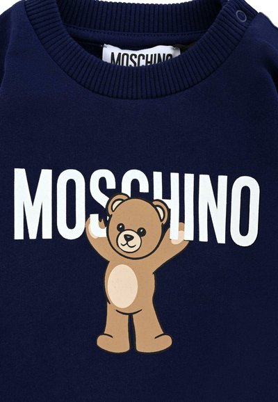 Felpa blu navy con colletto a coste, caratterizzata da un orsetto dei cartoni animati e "MOSCHINO" in bianco, evidenziato contro il tessuto.