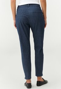Pantalones ajustados de color azul oscuro, con un corte slim, textura suave y diseño de dos bolsillos en la parte trasera. Combinados con bailarinas negras.