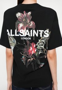 T-shirt in cotone nero con design floreale in rosso, bianco e verde, con la scritta "ALLSAINTS LONDON" in bianco bold sulla schiena.