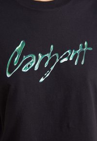 Camiseta negra con un diseño de texto abstracto verde brillante, con una textura suave y una forma clásica de cuello redondo.