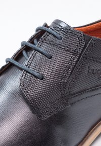 Chaussures en cuir noir avec un panneau texturé, des lacets ronds et une finition lisse, dotées d'un intérieur contrastant marron et de détails de design minimalistes.