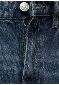 Gros plan de la ceinture d’un jean en denim bleu foncé avec bouton métal visible, fermeture éclair, boutonnière et surpiqûres orange contrastantes.