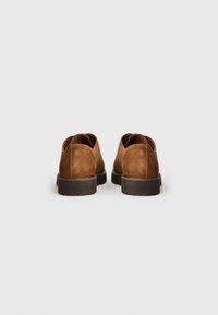 Scarpe in suede marrone con forma arrotondata, tacco basso e suole testurizzate. Presentano dettagli cuciti e un design semplice.