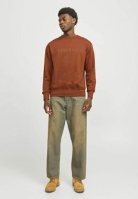 Sudadera de forro polar marrón con texto en relieve "ORIGINALS", combinada con vaqueros de pierna ancha de color claro y botas elegantes de color marrón claro. Diseño simple y casual.