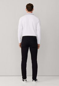 Camisa polo blanca de manga larga con cuello a rayas en negro y azul, combinada con jeans negros ajustados y zapatillas blancas.