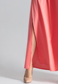 Korallenfarbenes Satin-Maxi-Kleid mit einem Seitenschlitz, das eine glatte Textur aufweist. Kombiniert mit nude-farbenen High Heels, die die Länge des Kleides betonen.